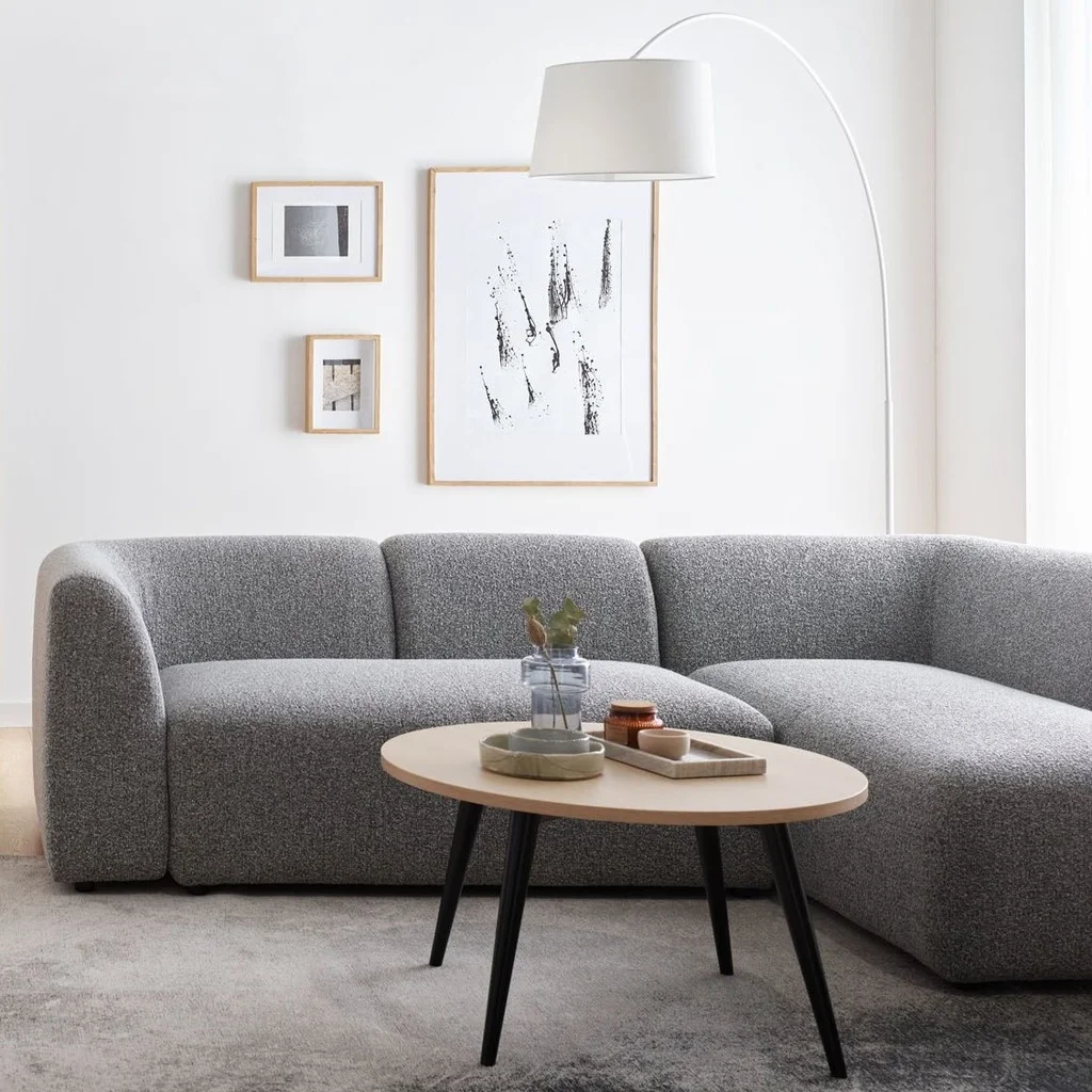 Minimalistyczny salon z szarą sofą i białymi ścianami.